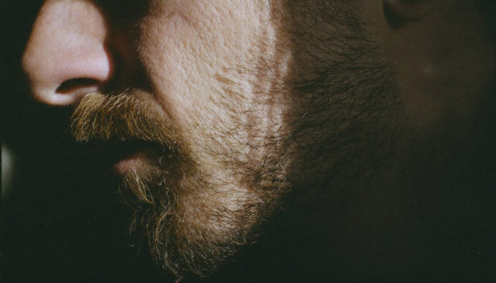 Man examining dry skin beneath beard in bathroom mirror - skin barrier repair for bearded men